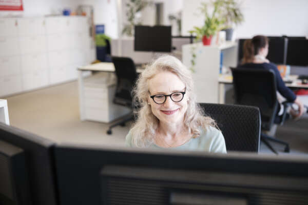Eine Frau sitzt an einem Computer im Büro und lächelt.