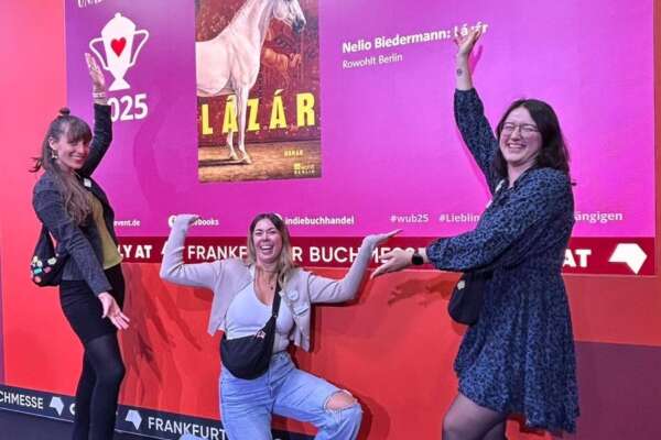 Drei Frauen vor einer Leinwand mit dem Cover vom Gewinner-Buch des Lieblingsbuch der Unabhängigen 2025.