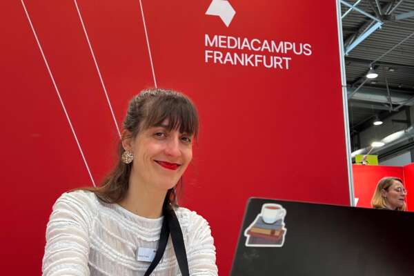 Eine Frau sitzt vor einem Laptop am Stand des Börsenvereins und lächelt in die Kamera.