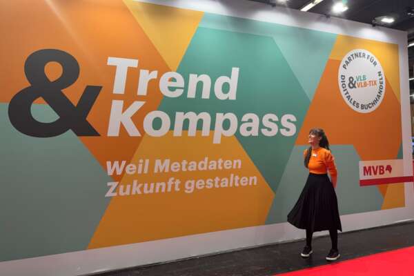Eine Frau steht vor einer Messewand mit der Aufschrift Trend und Kompass.
