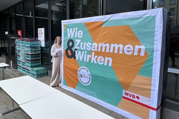 Frau steht neben einer Marketing Wand mit dem Aufdruck "Wie Zusammen und Wirken".