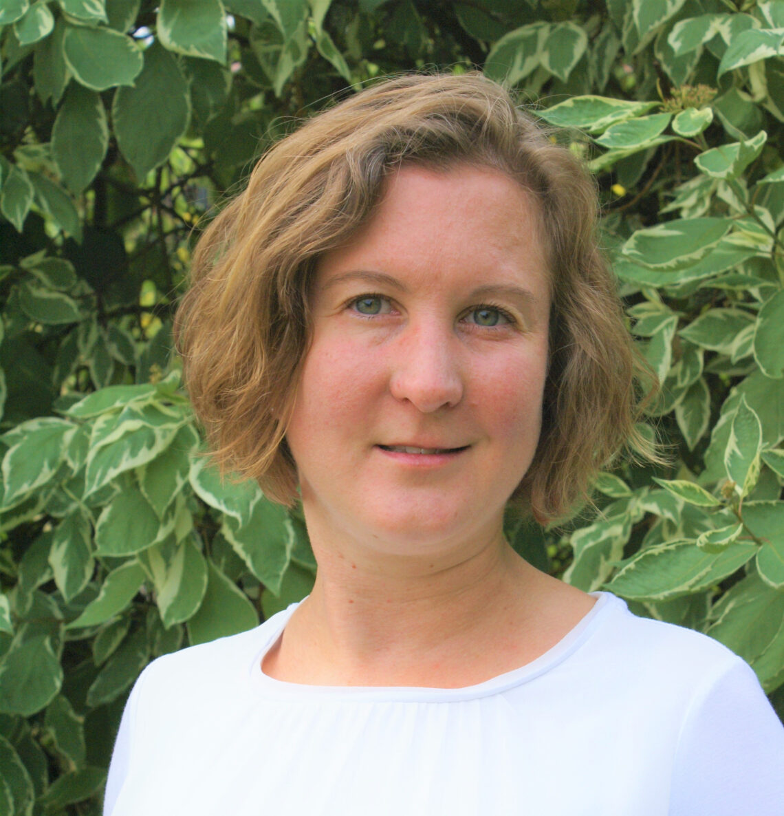 Porträt von Christine Heidkamp vor einer grünen Hecke.