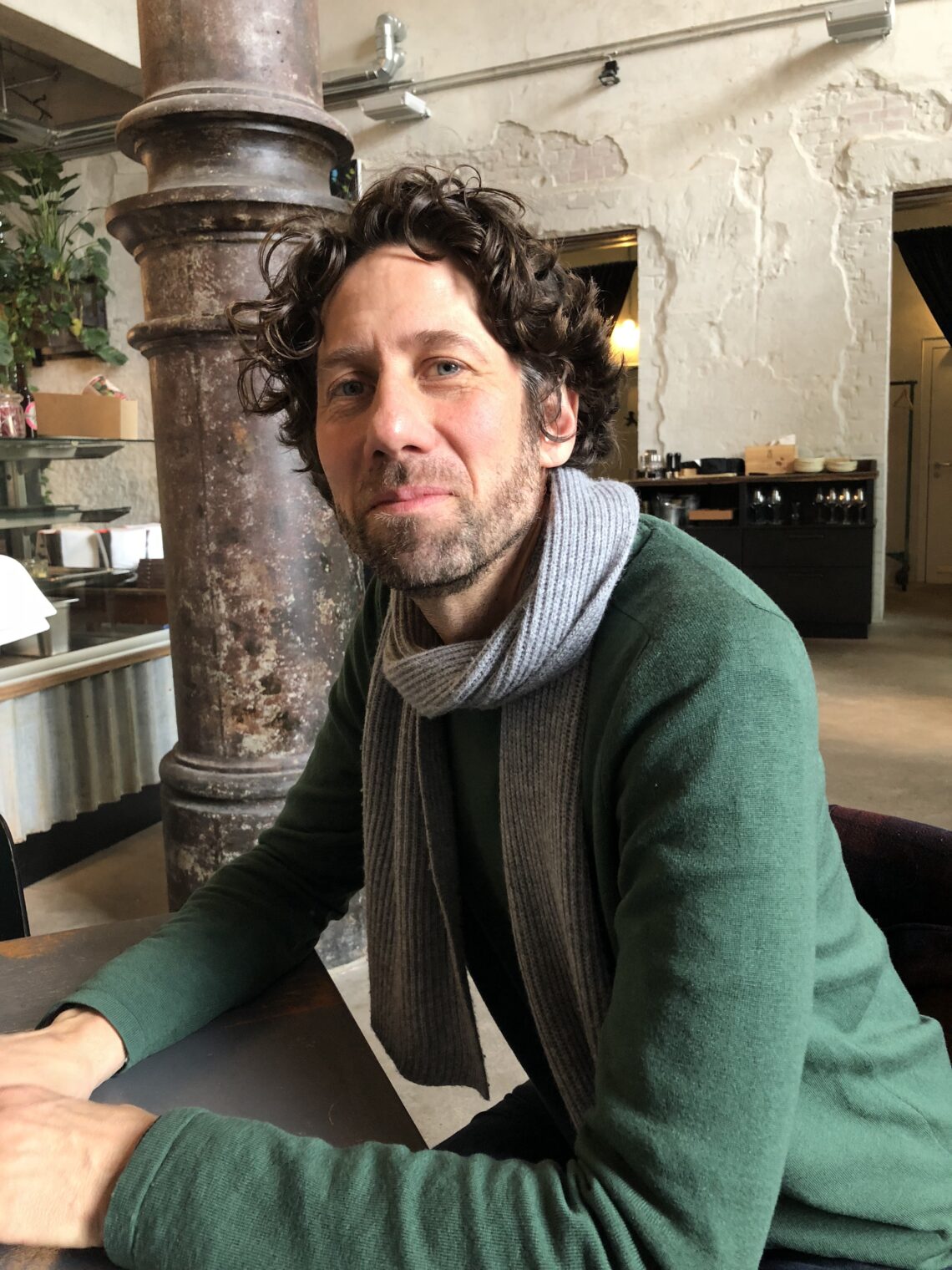 David Mesche im seitlichen Profil der an einem Tisch sitzt und in die kamera schaut.