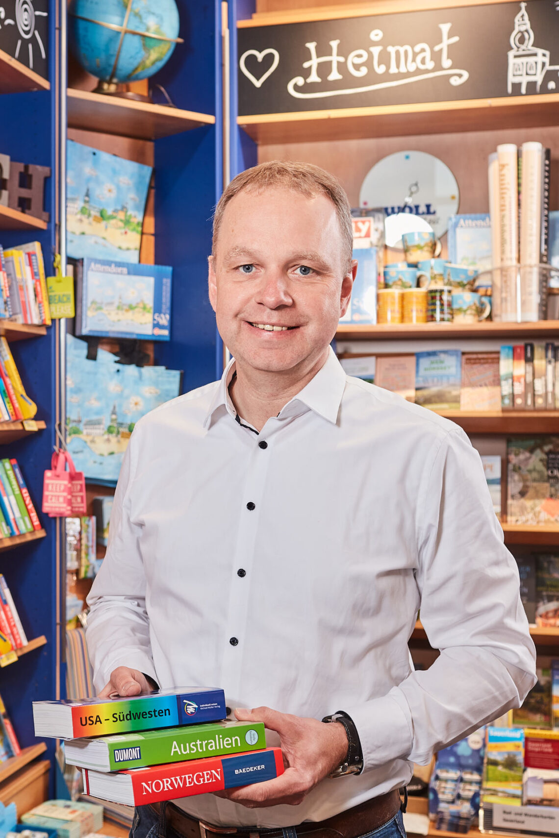 Michael Frey aus der Buchhandlung Frey mit einem Stapel Bücher in der Hand vor einem Bücherregal.