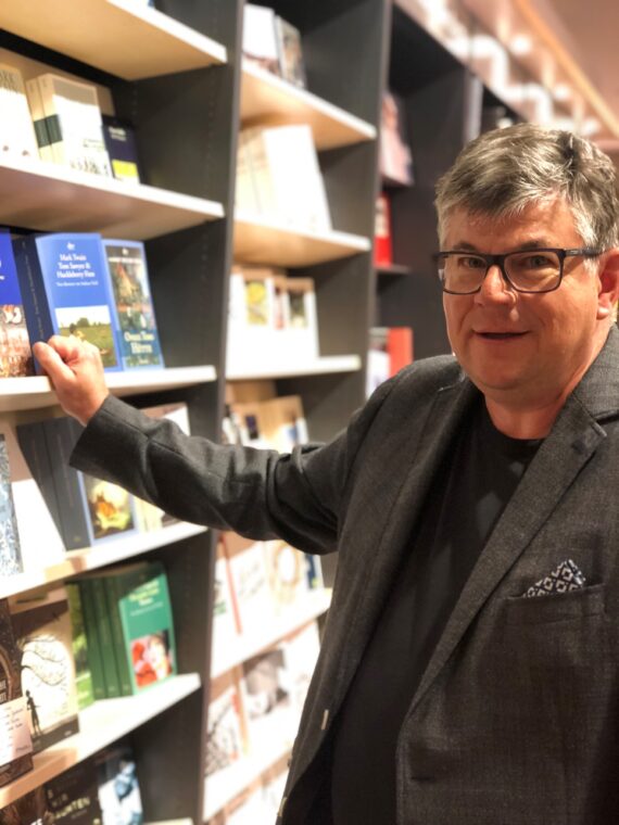 Porträt von Matthias Kuhlemann der mit einer Hand an einem Bücherregal lehnt.