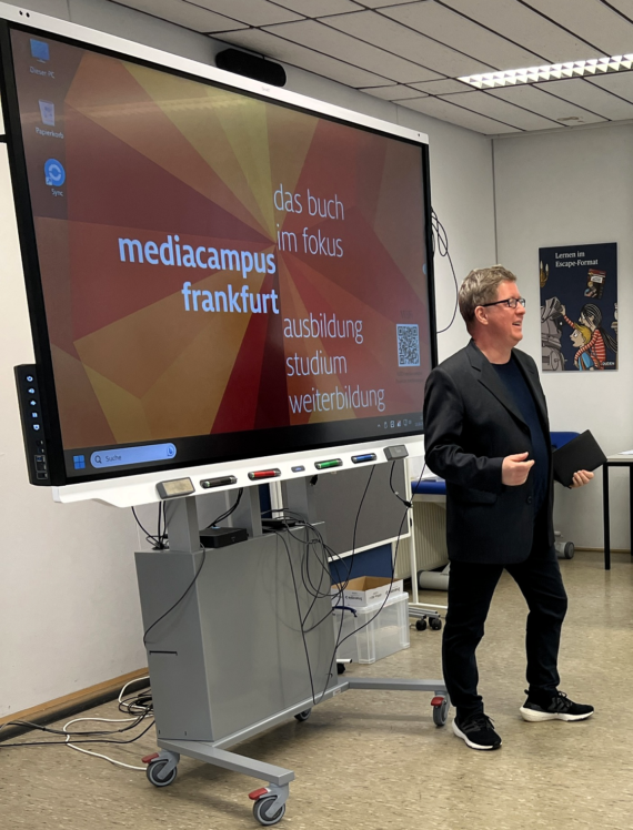 Patrick Musial neben einer digitalen Tafel im Klassenraum am mediacampus in Frankfurt.
