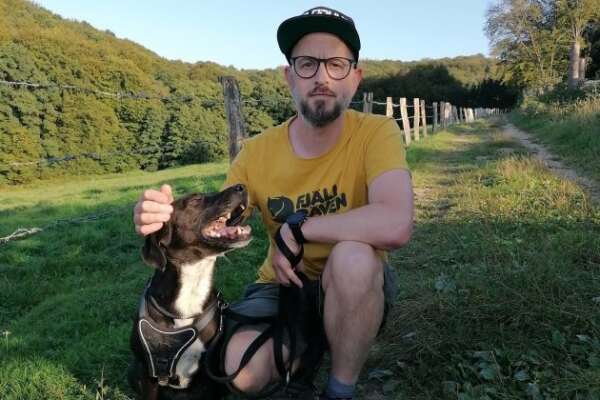 Boris Langner hockt auf einer Wiese, neben ihm sitzt ein Hund der zu ihm aufschaut.