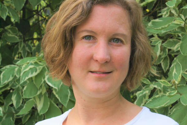 Porträt von Christine Heidkamp vor einer grünen Hecke.