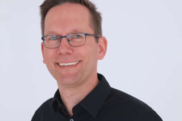 Porträt von Marc Janeczek vor einer weißen Wand.