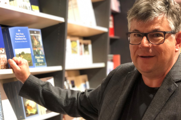 Porträt von Matthias Kuhlemann der mit einer Hand an einem Bücherregal lehnt.