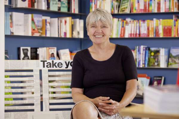 Sabine Gartmann sitzt in der Buchhandlung Die Schatulle vor einem Bücherregal und lächelt.