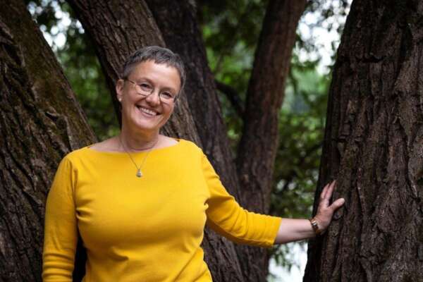 Verena Boettger lehnt lächelnd mit einer Hand an einem Baum.