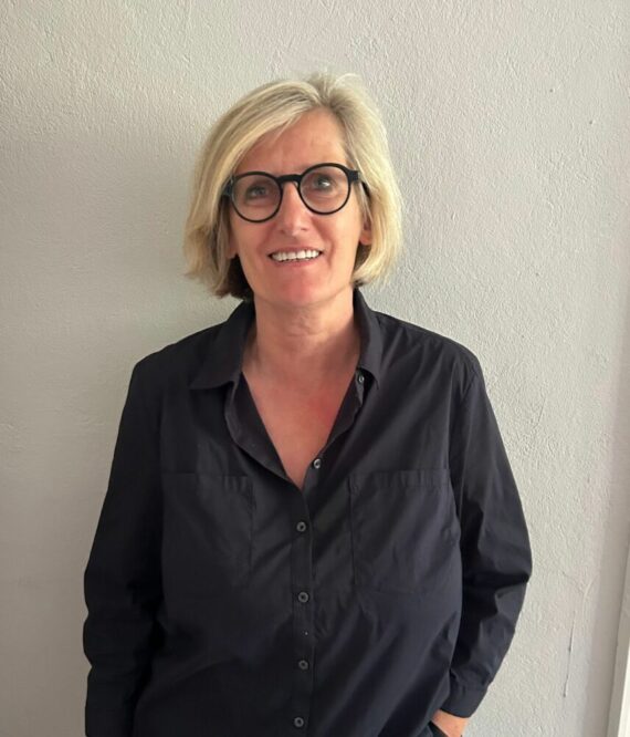 Christiane Hoffmeister steht für ein Foto posierend vor einer weißen Wand.