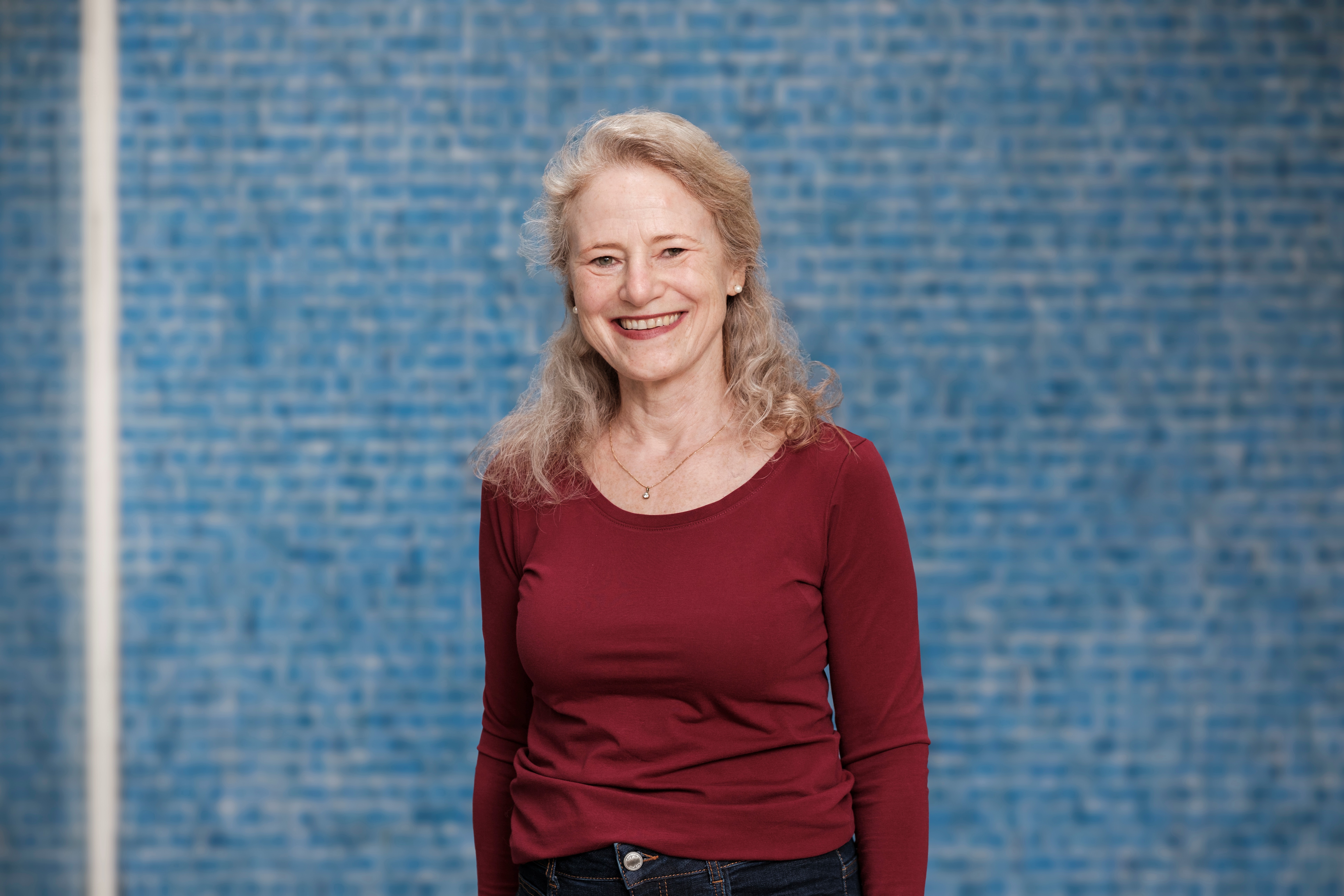 Lachendes Porträt von Susanne Fuchs vor einer dunkelblauen Mosaikwand.
