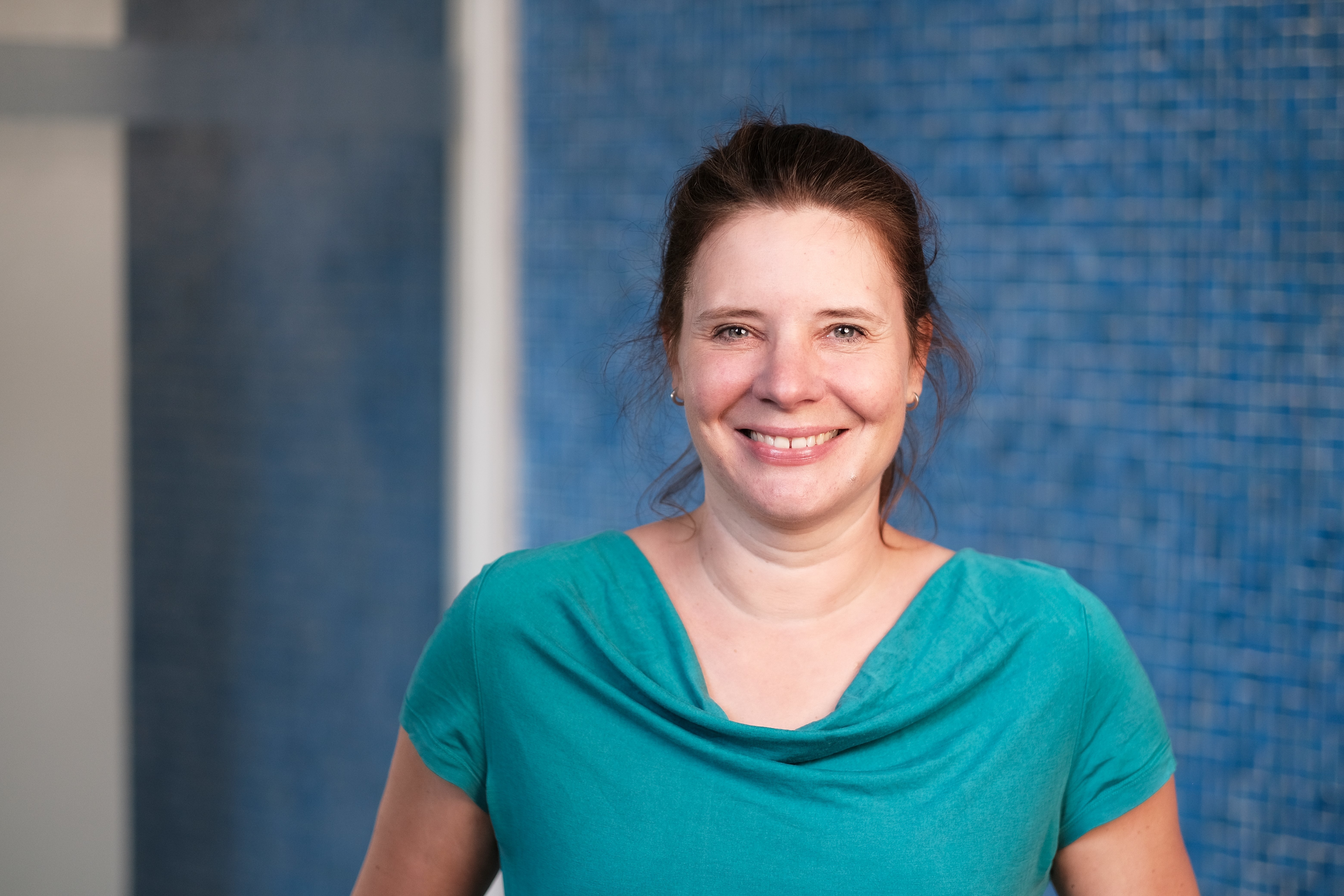 Lachendes Porträt von Daniela Kahl vor einer dunkelblauen Mosaikwand.