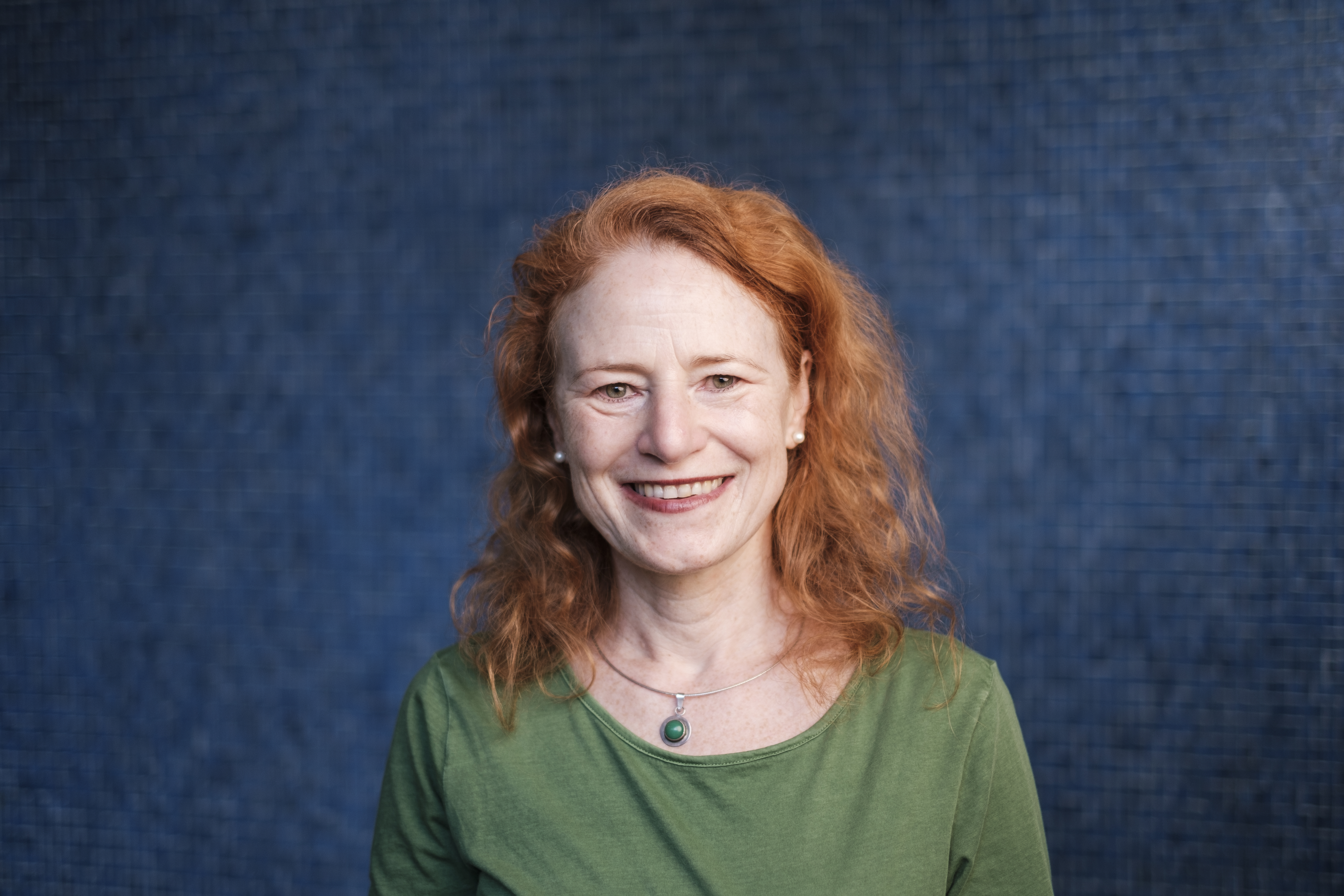 Lachendes Porträt von Susanne Fuchs vor einer dunkelblauen Mosaikwand.