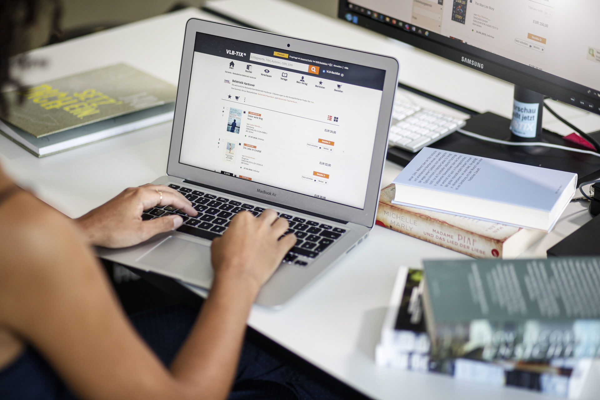 Blick über eine Schulter auf einen Laptop mit einer Hand auf der Tastatur und der Web-Oberfläche von vlbtix.de.