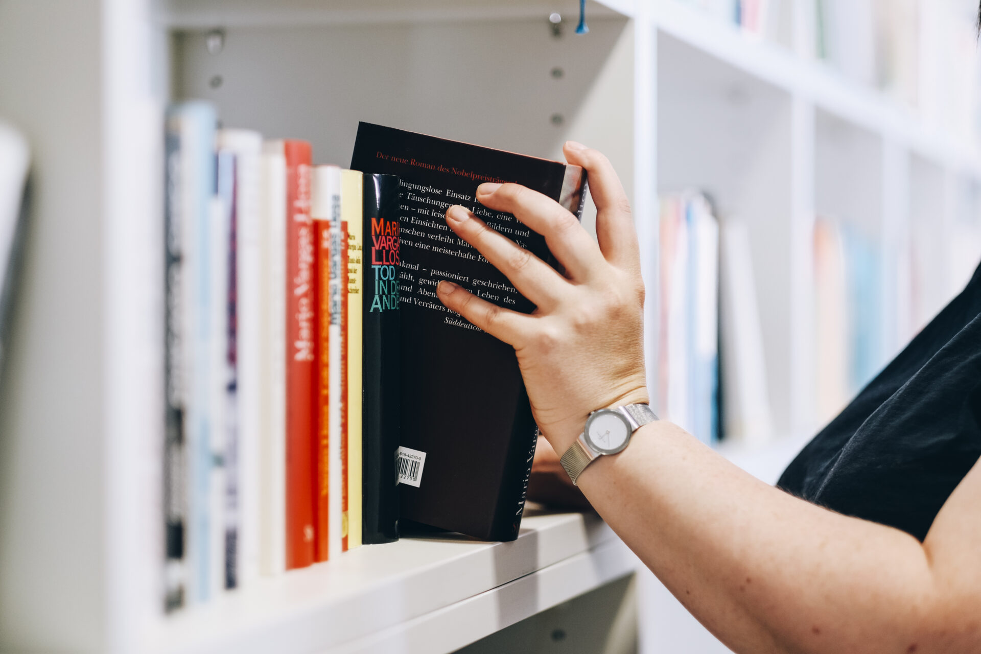 Eine Hand zieht ein Buch aus einem Bücherregal heraus.