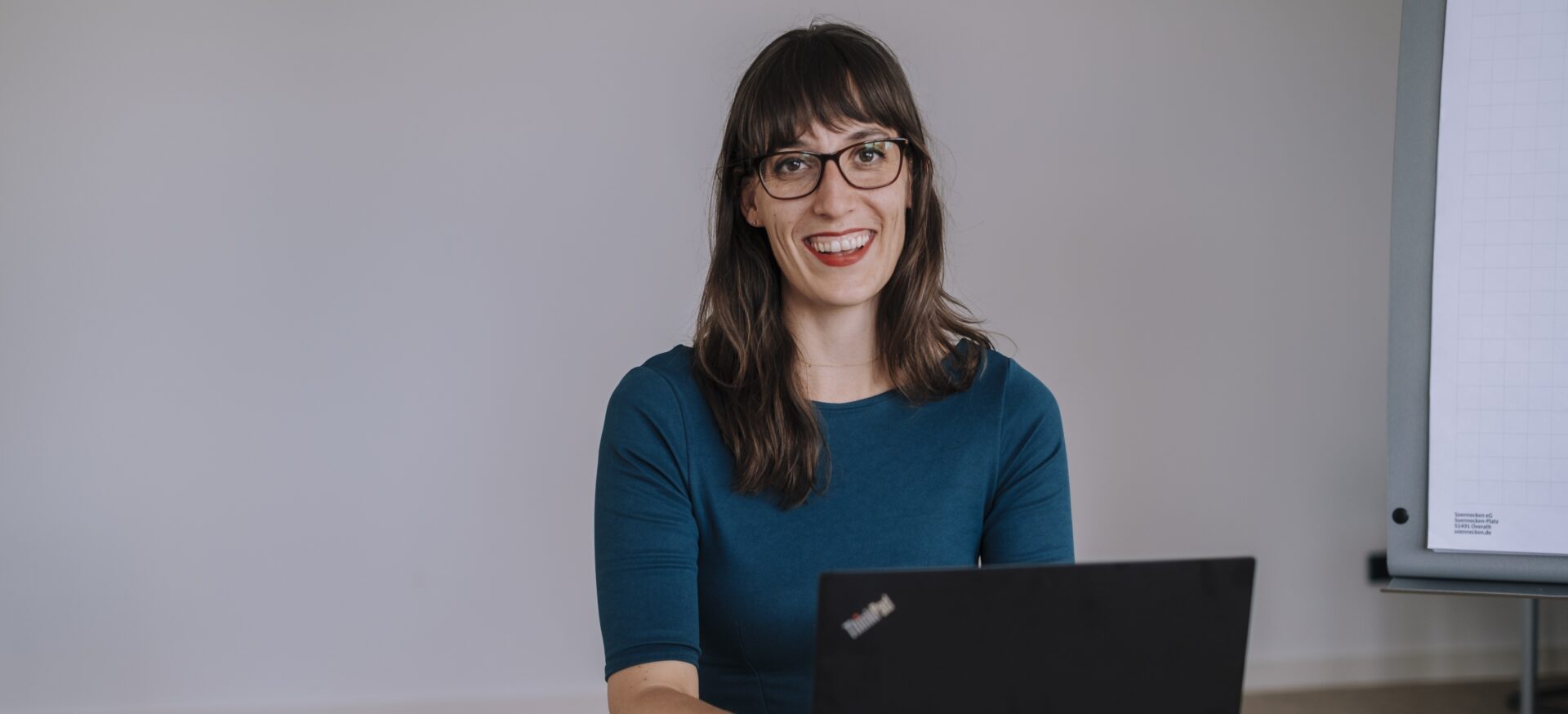 Eine Frau sitzt in einem Arbeitsraum an einem Tisch vor einem offenem Laptop.