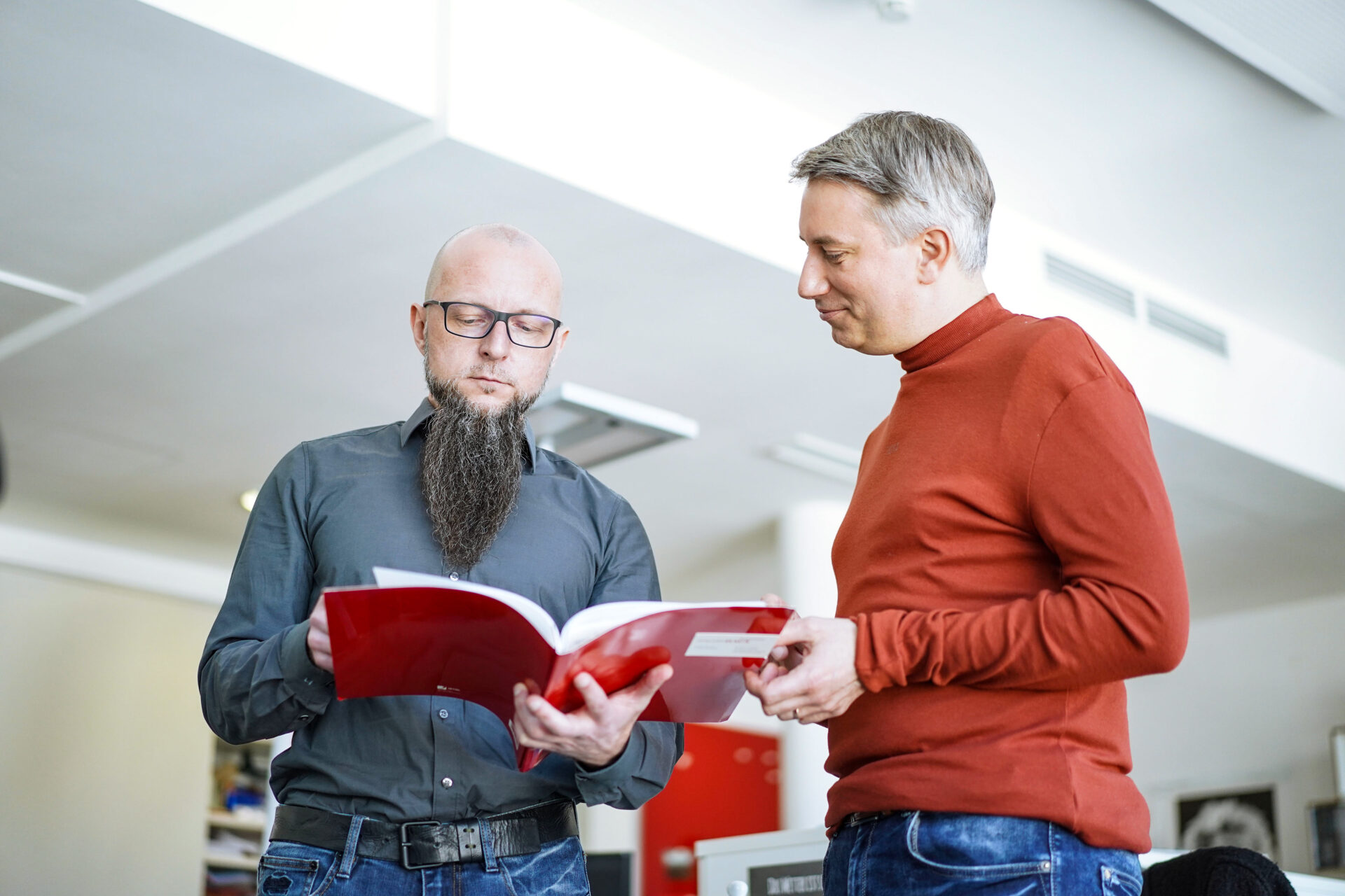 Zwei Männer stehen in einem Büro und haben einen Katalog in der Hand.