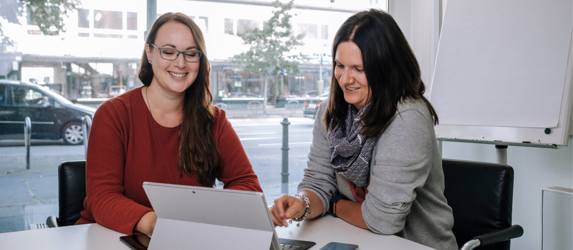 Zwei Frauen sitzen an einem Tisch vor einem offenem Laptop.