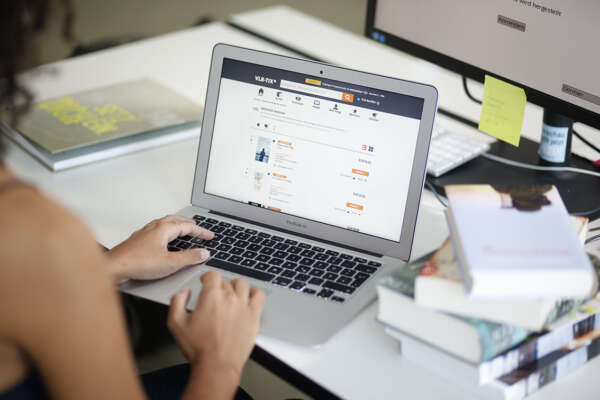 Blick über eine Schulter auf einen Laptop mit einer Hand auf der Tastatur und der Web-Oberfläche von vlbtix.de.