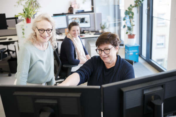 Das Vertriebsteam Susanne Fuchs, Eva Singer und Daniela Kahl gucken gemeinsam auf einen Bildschirm.