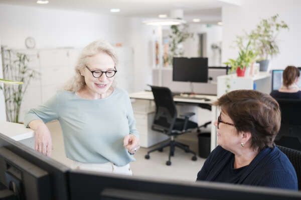 Zwei Frauen unterhalten sich am Bildschirmarbeitsplatz