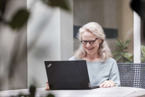 Eine Frau sitzt vor einem Laptop an einem Tisch und arbeitet.