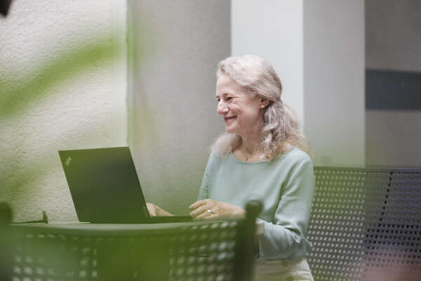 Eine Frau sitzt vor einem Laptop an einem Tisch und arbeitet.