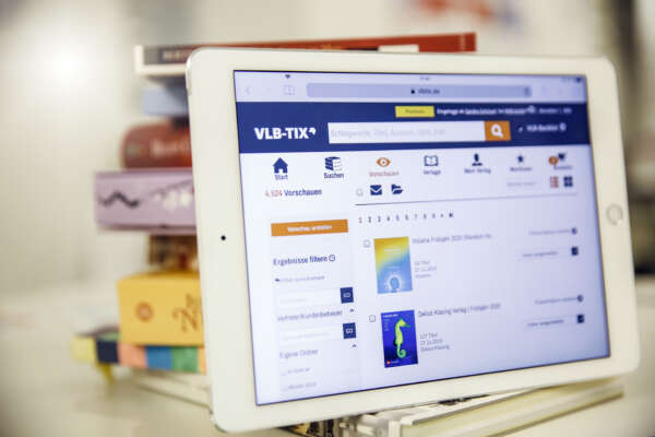 Ein Tablet mit der geöffneten Webseite von VLB-TIX lehnt gegen einen Stapel Bücher.
