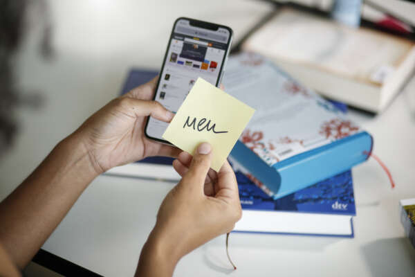 Zwei Hände halten ein Smartphone und ein Post-It auf dem die Webseite von VLB-TIX aufgerufen ist.