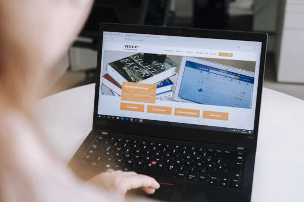 Eine Frau arbeitet an einen Laptop auf dem die Webseite von VLB-TIX aufgerufen ist.
